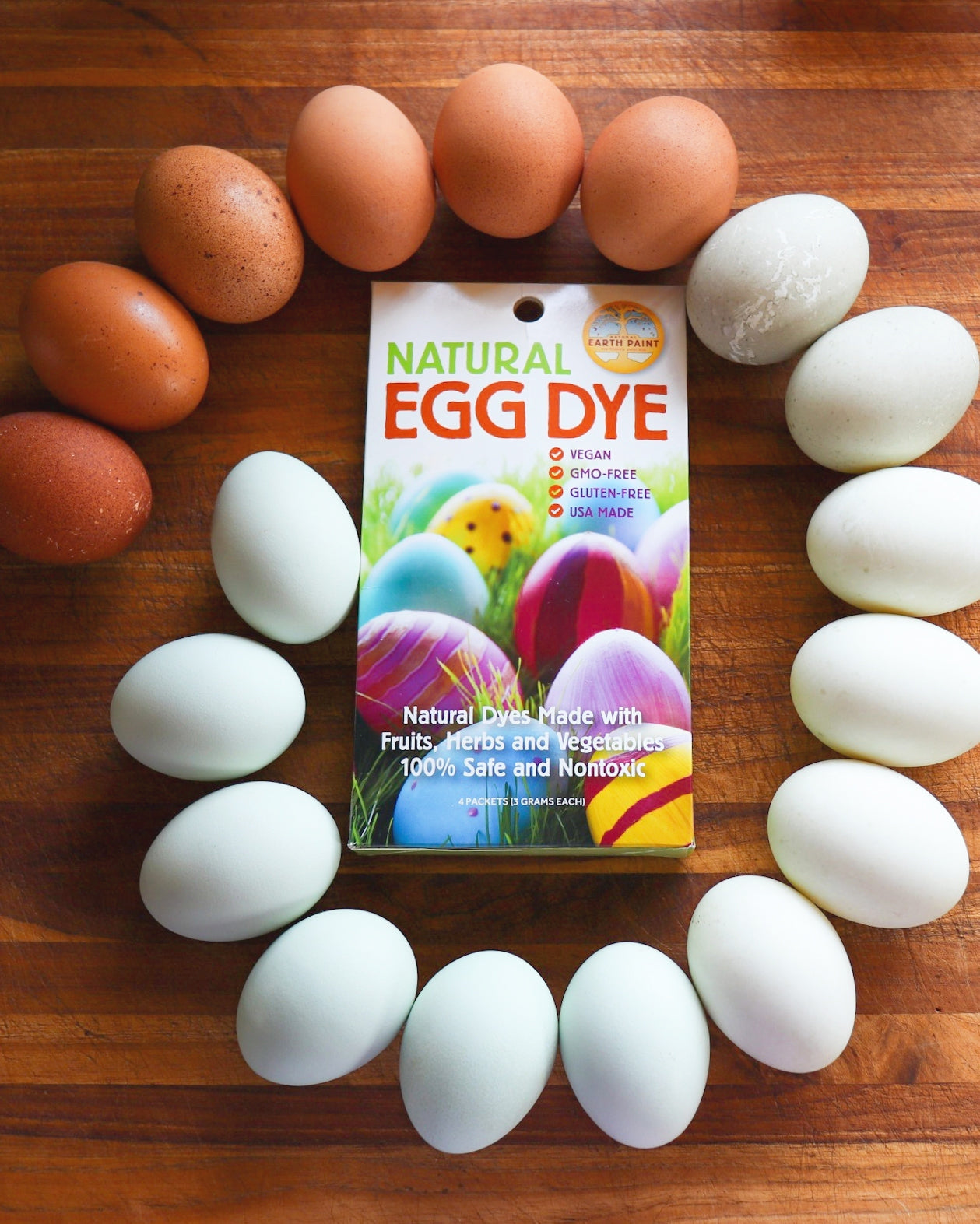 Spiral of eggs laid on a wooden table, encircling NEP's Natural Egg Dye Kit, ranging from colors white to brown