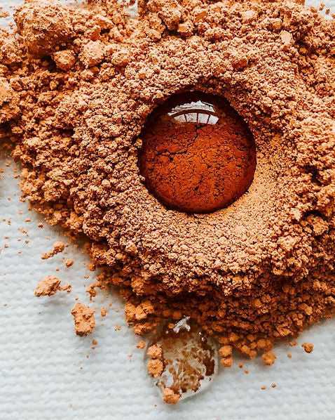 A drop of liquid nesting in a pile of brown pigment on a glass palette
