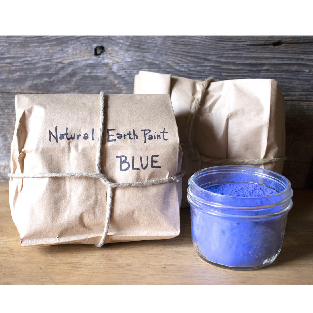 Two paper bags secured with twine containing Natural Earth Paint next to an open jar of the same