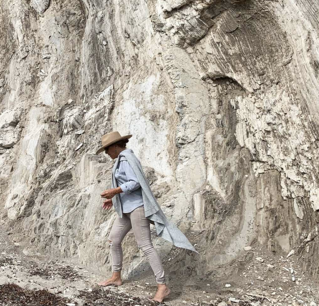 Artist Christine Aspergren walking in front of a large rock face, collecting natural minerals.