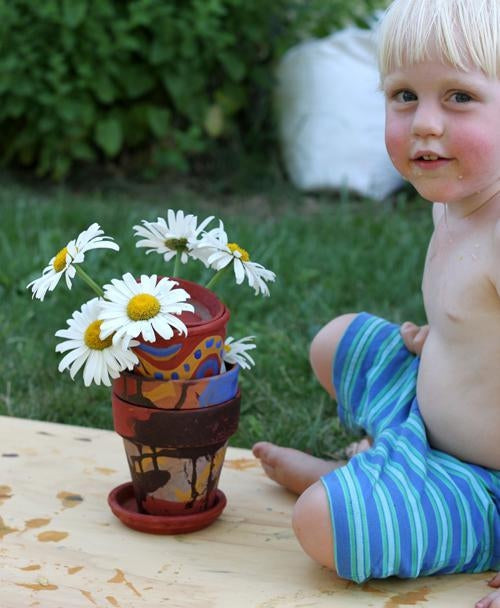 Yound child sitting next to a stack of colorfully painted clay pots with white daiseys sticking out of the top one.