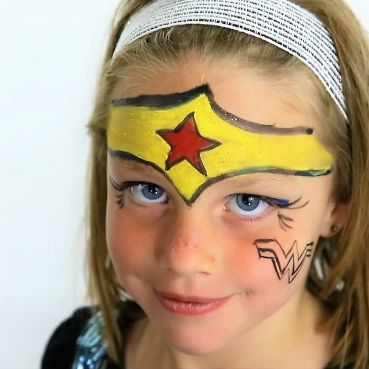 Young girl's face painted with Wonder Woman headband on forehead and logo on cheek