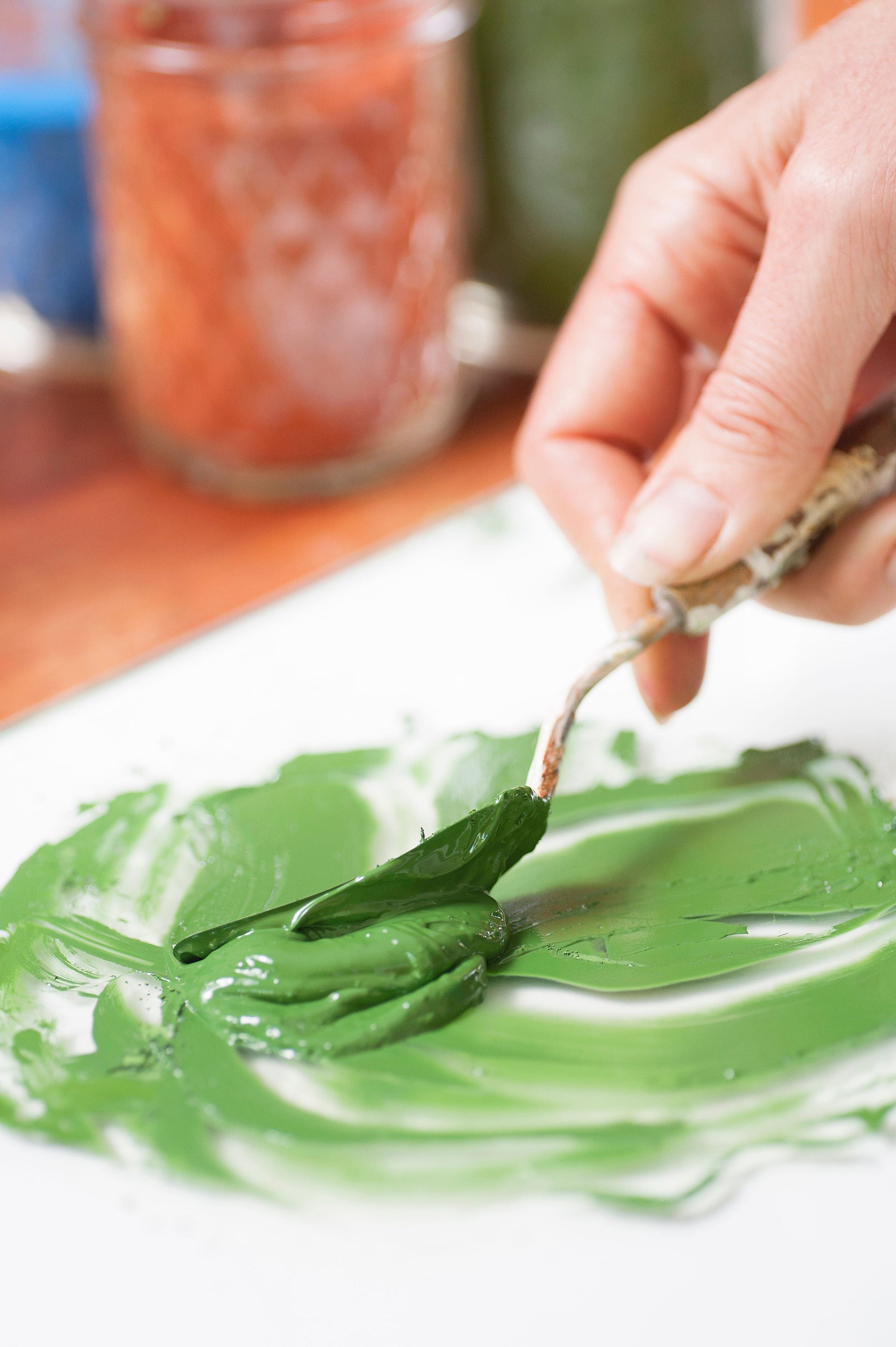 hand holding a palette knife mixing up green natural oil paint on a glass palette