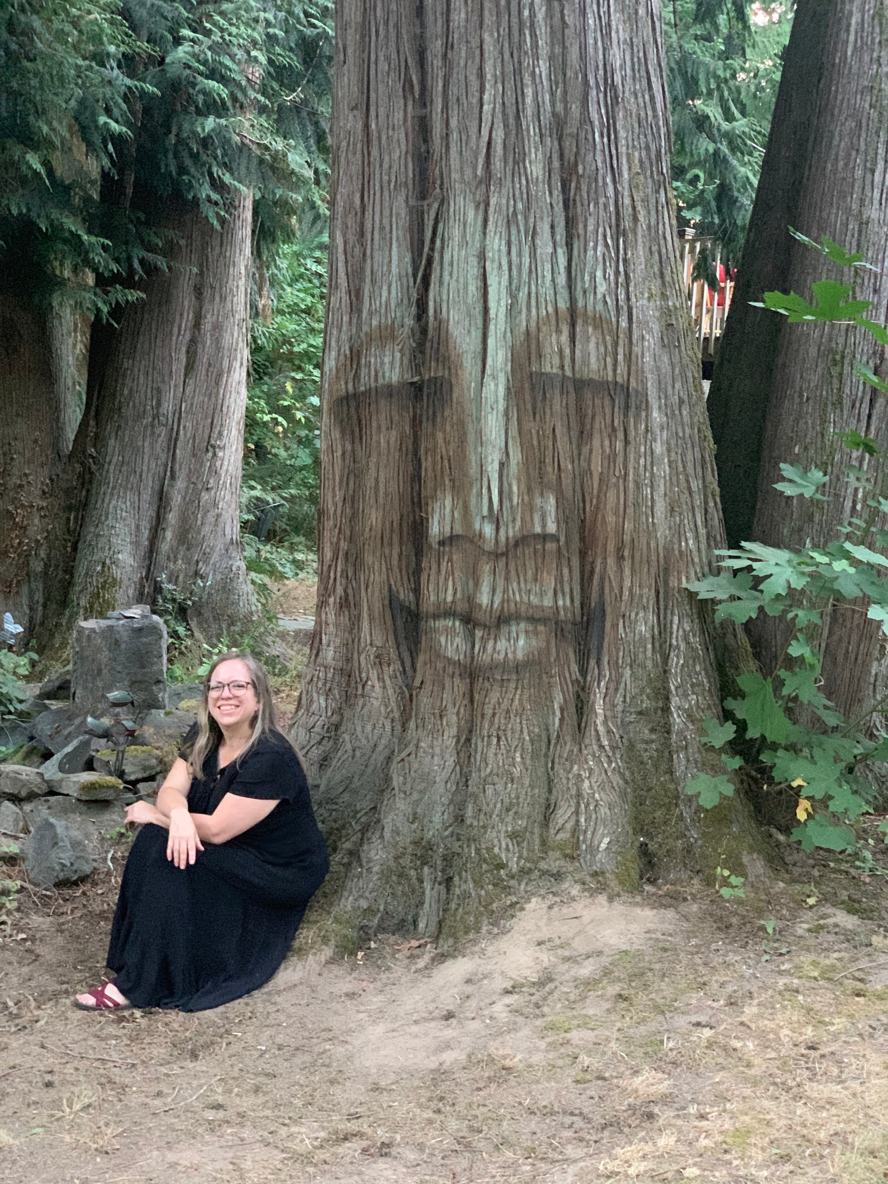 Artist Erica Gibson sitting on the ground at the base of a large tree they have painted with Natural Earth Paints