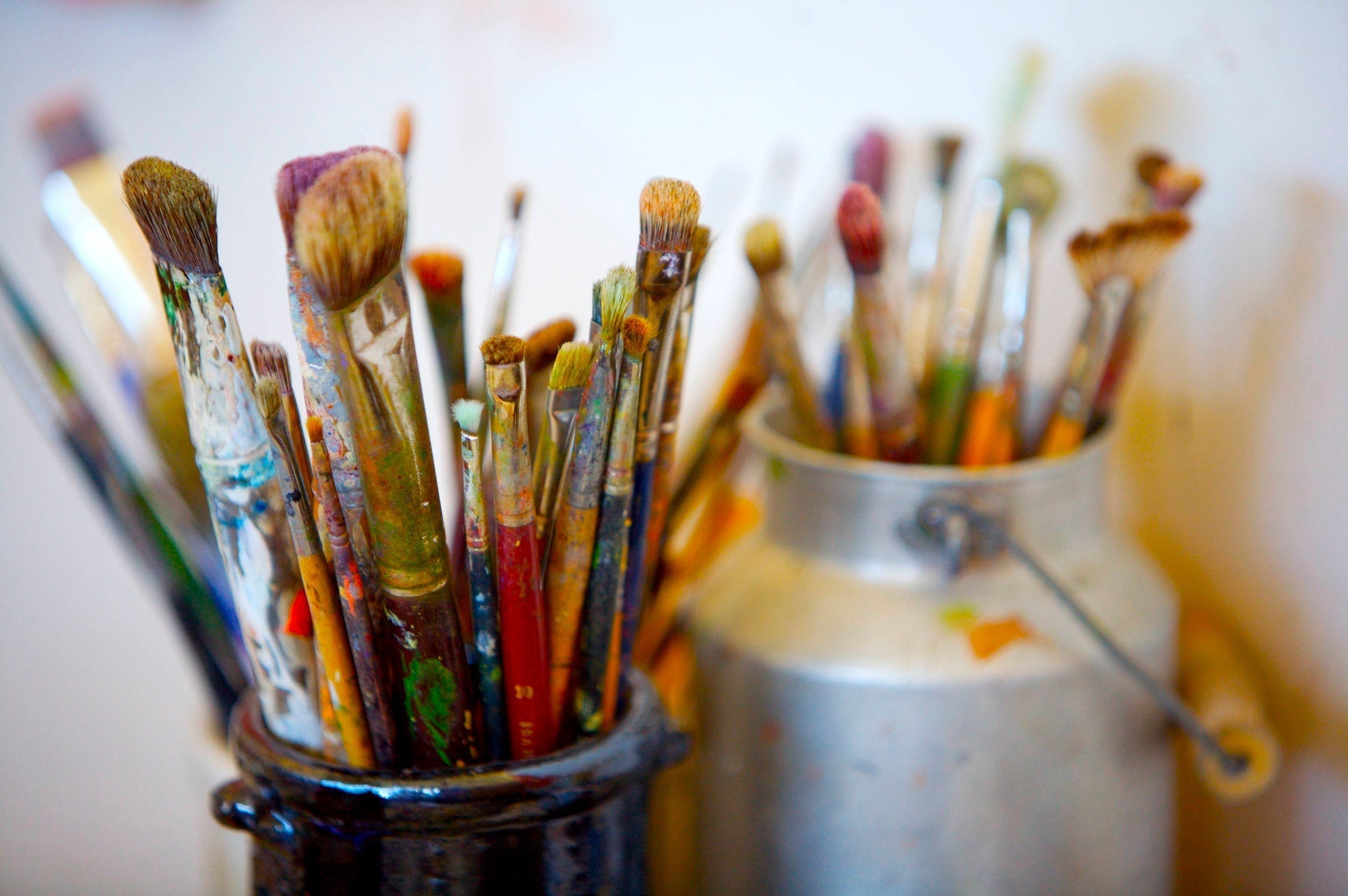 Two containers holding a wide array of various shapes and sizes of paint brushes