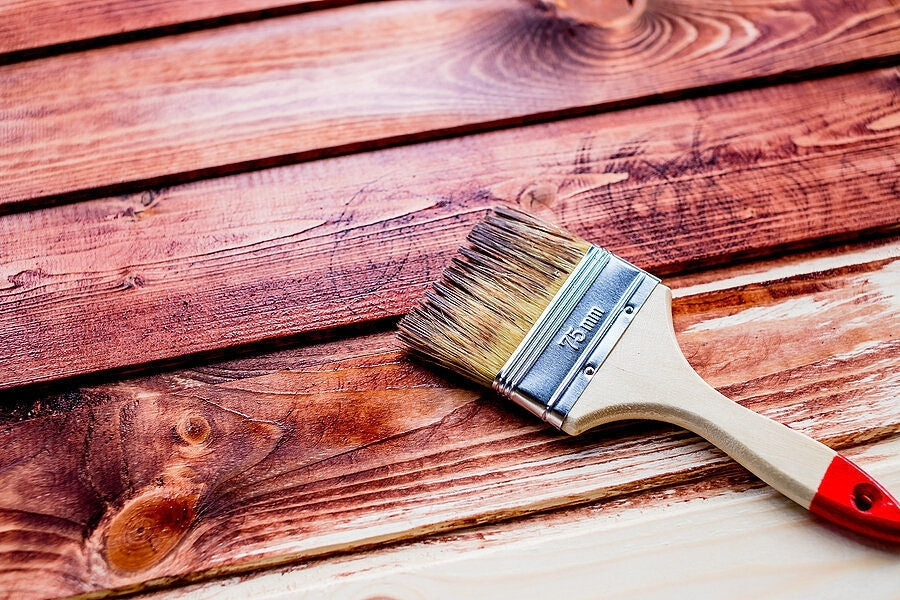 Pieces of wood that are being stained a red-ish color with Earth & Mineral Pigments with a paint brush laid on top of the wood