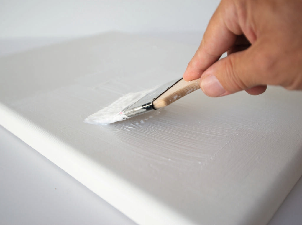 Close up photo of hand applying gesso to a canvas with a medium brush