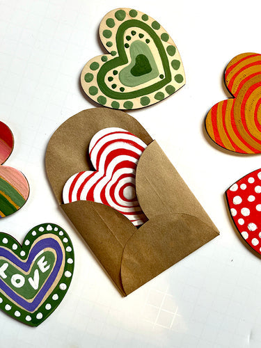 Image of beautifully painted hearts, and one of them is peeking out from inside a custom eco-friendly envelope