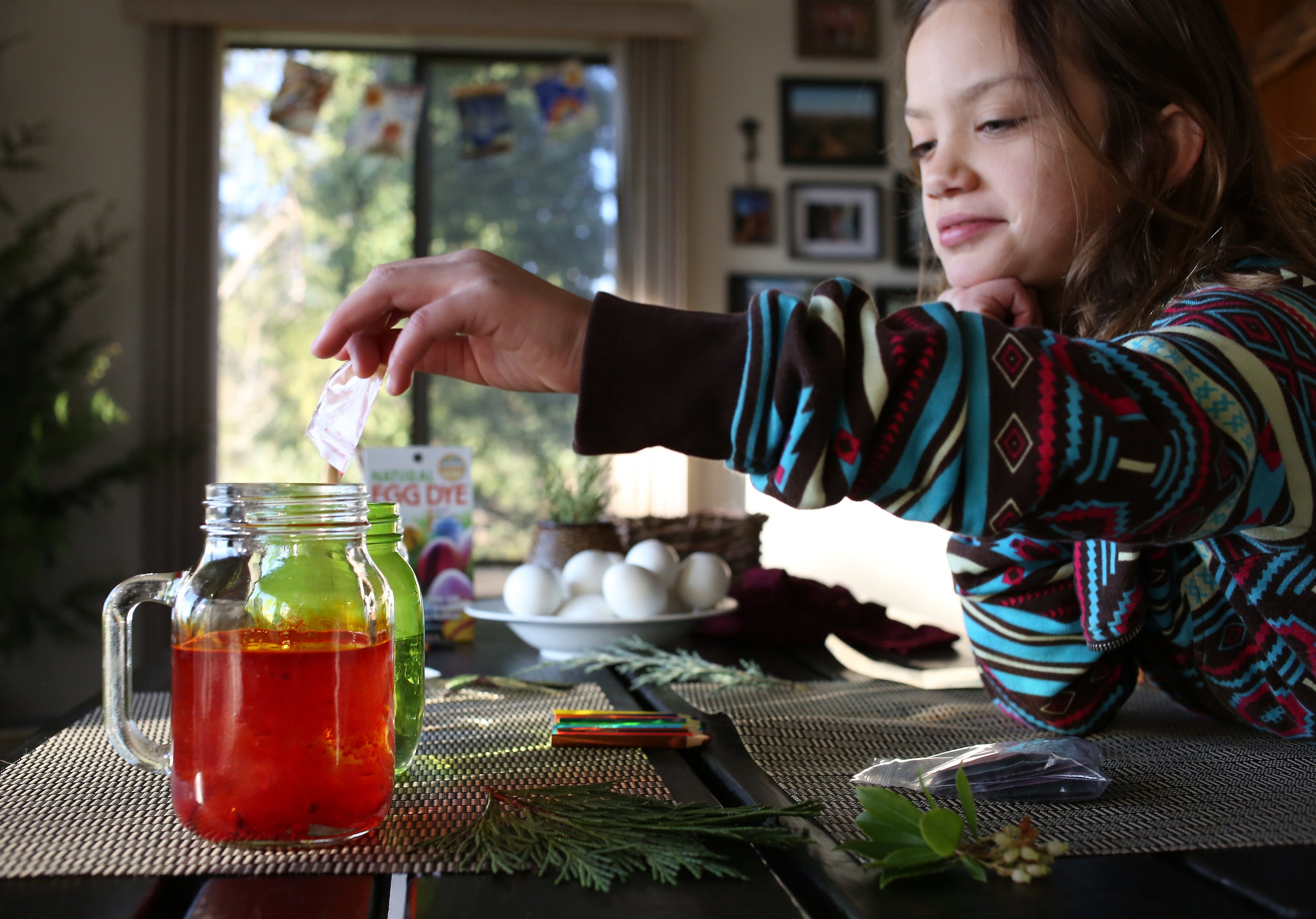 child reaching their hand to dig an egg into a glass jar filled with red Natural Egg Dye 