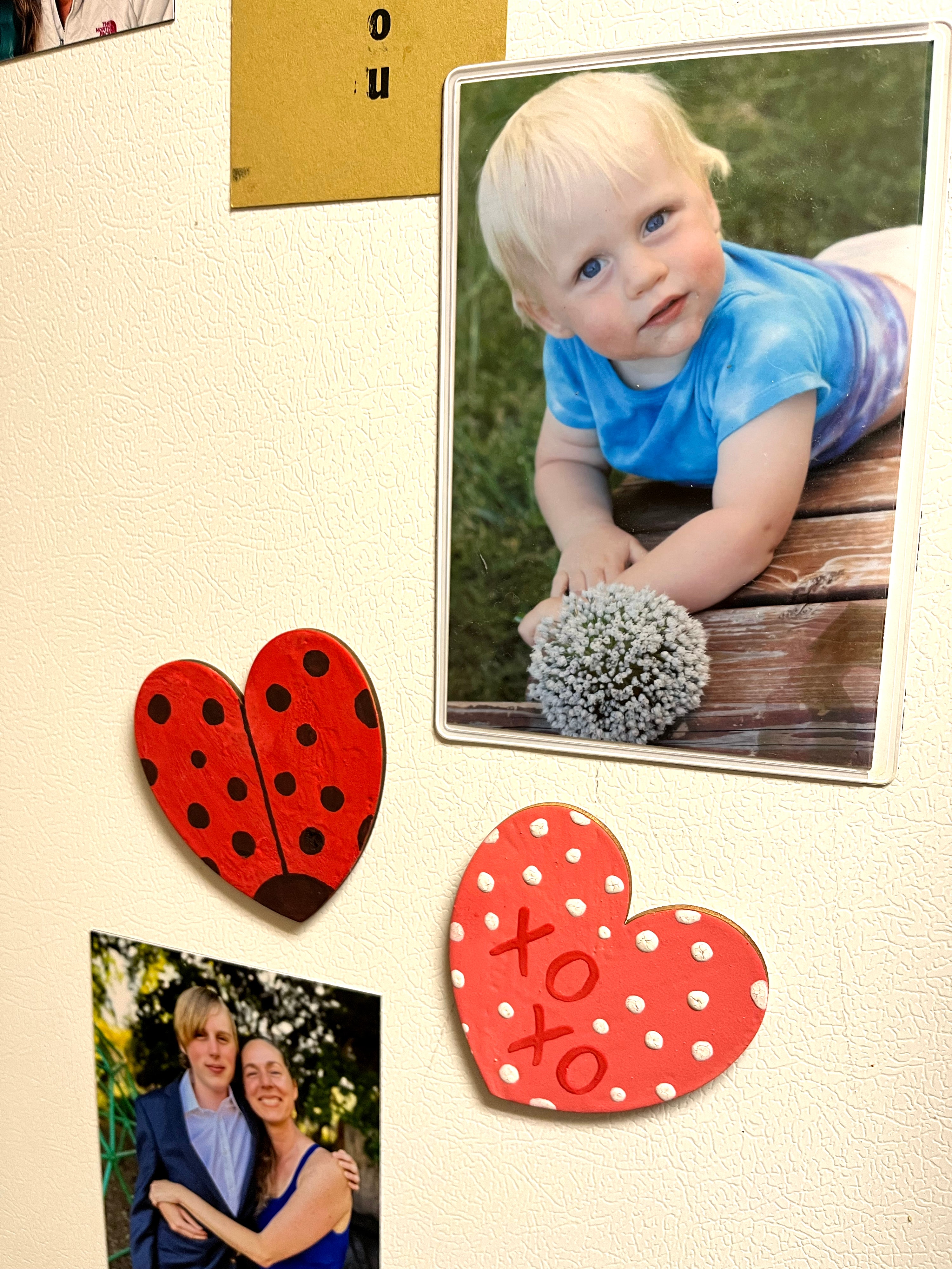 Painted heart magnets on a fridge next to personal photographs