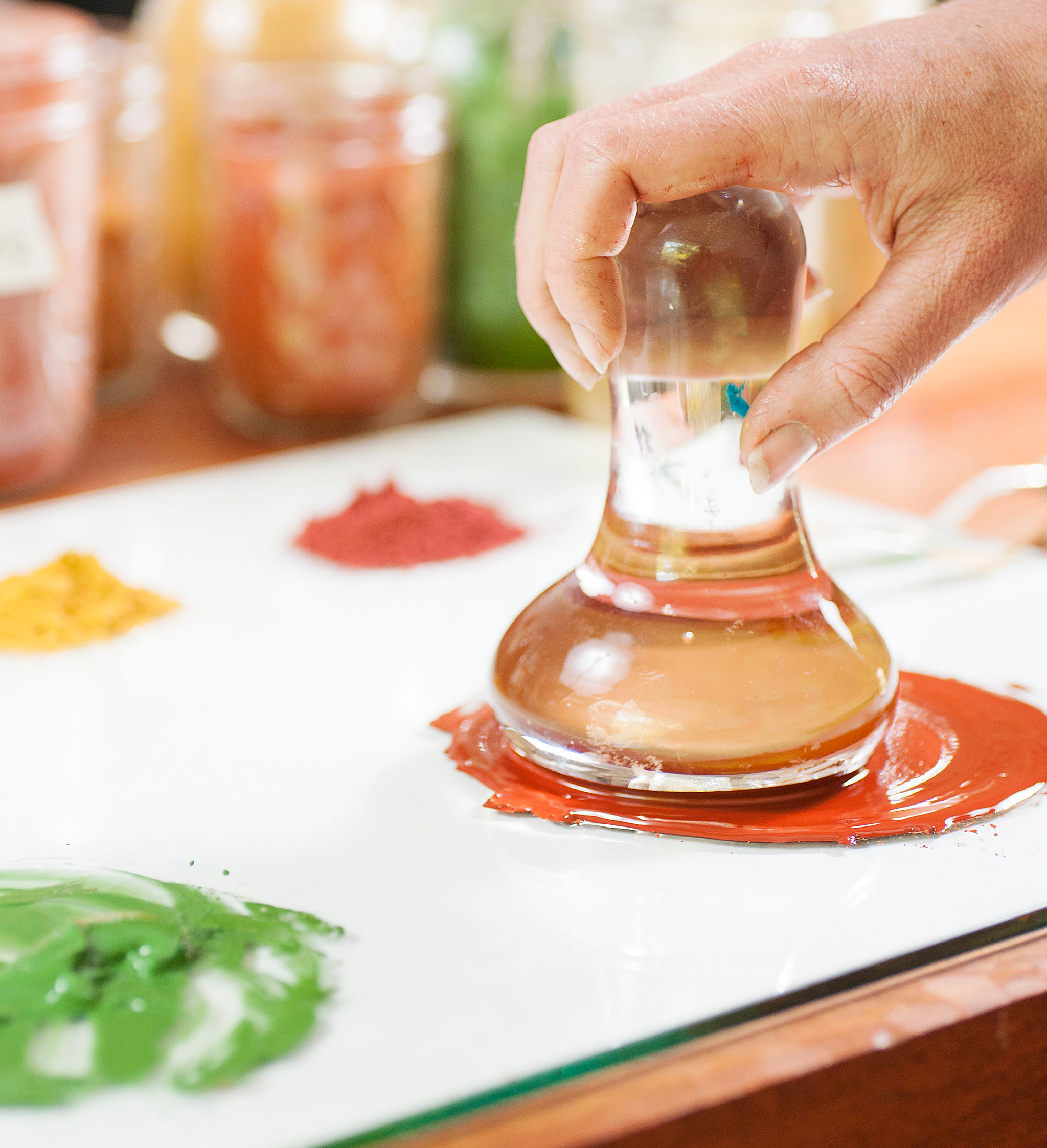 Person using a glass muller to mix up red paint on a glass palette