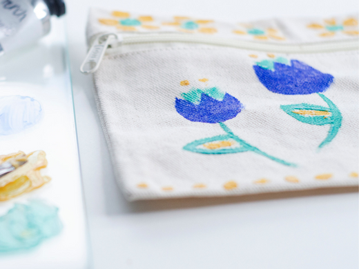 A canvas zipper pouch with flowers and designs painted on it using Natural Acyrlik Paint colors blue, green and yellow.