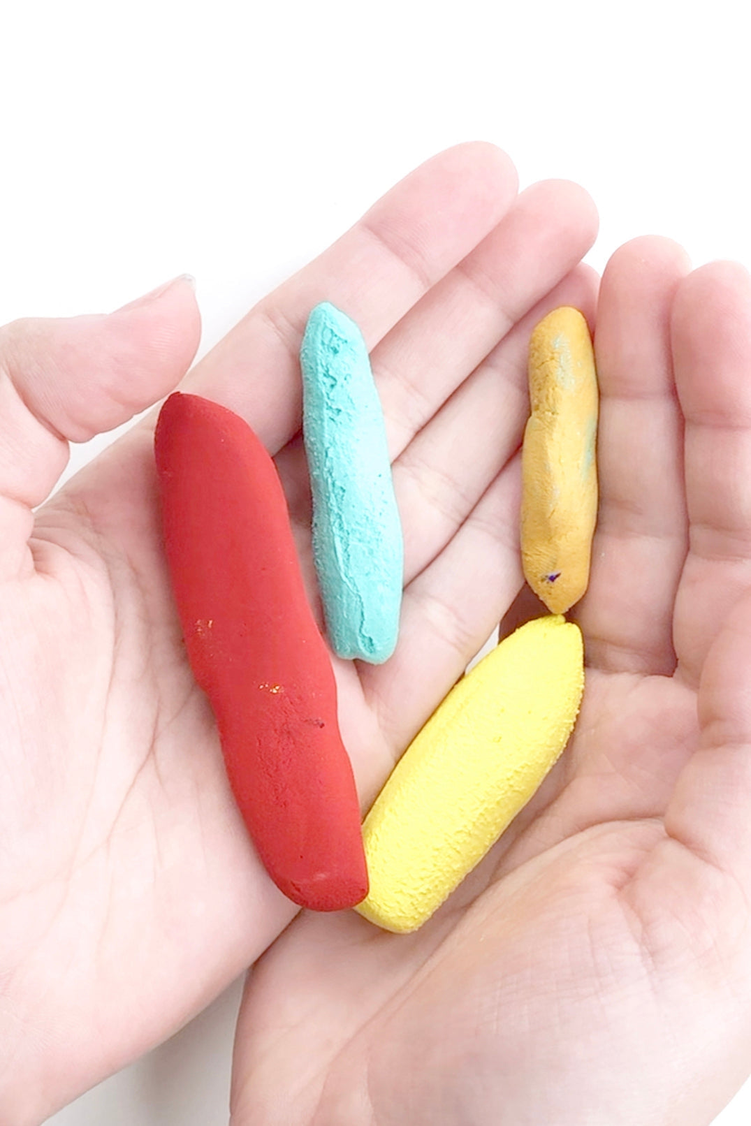 Person's hands holding 4 handmade chalk pastels (Red, turquoise, light yellow and medium yellow)