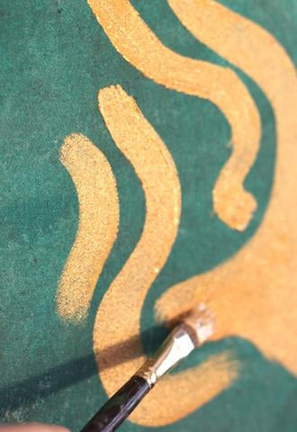 Green paper with gold paint and a person's holding a paint brush applying the gold paint 