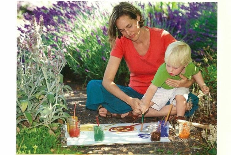 Photo of Natural Earth Paint found, Leah Fanning, sitting outside working on a painting with their child using various colors of Natural Earth Paint