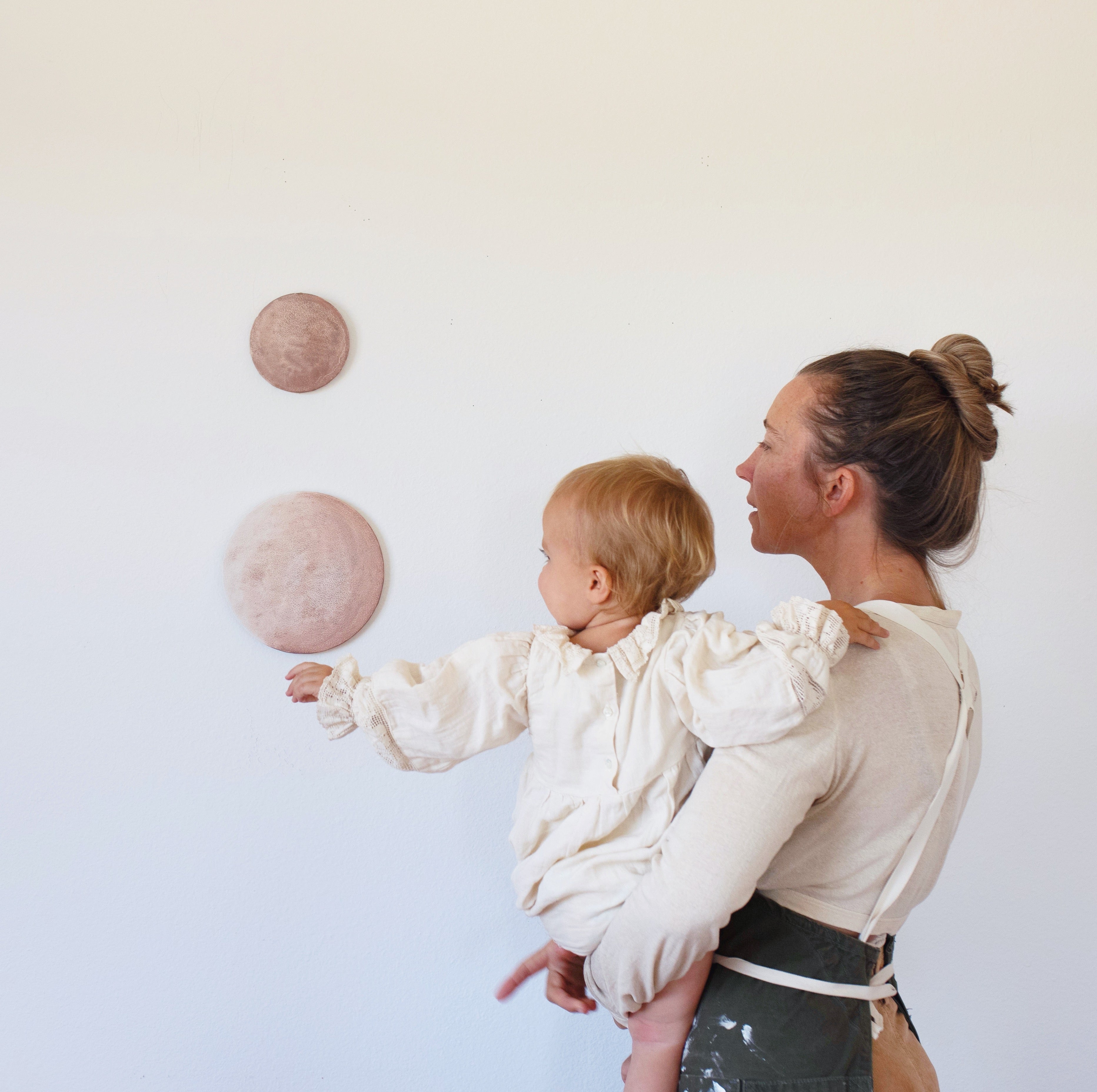 Portrait of mother and artist, Stella Maria Baer, standing in front of their work, holding their young child