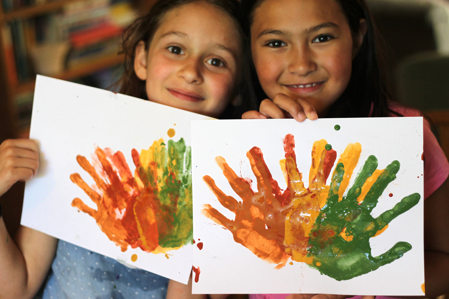 Two girls holding colorful paintings created using their hands 