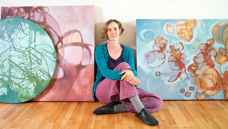 Artist and founder of Natural Earth Paint, Leah Fanning, sitting on the ground next to two large scale canvas paintings created using natural earth pigments