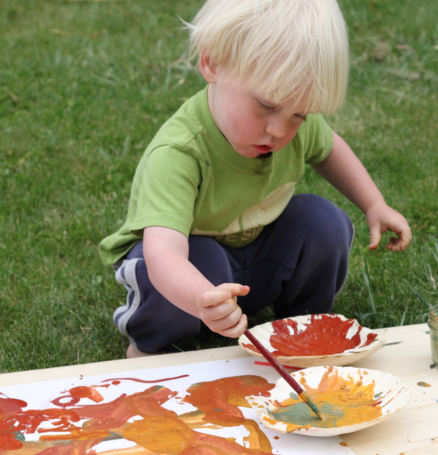 Young boy painting outside using Natural Earth Paint (yellow and orange) with a paint brush