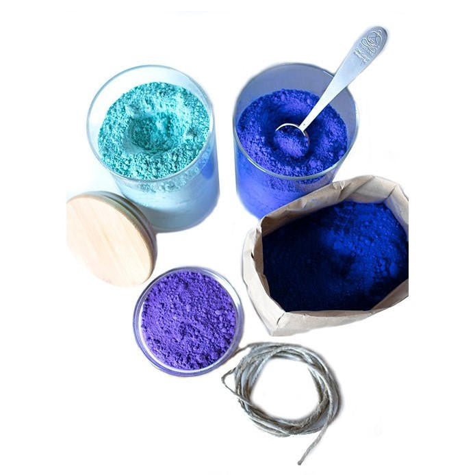 Aerial view of three glass jars and a paper bag containing various cool shades of pigment