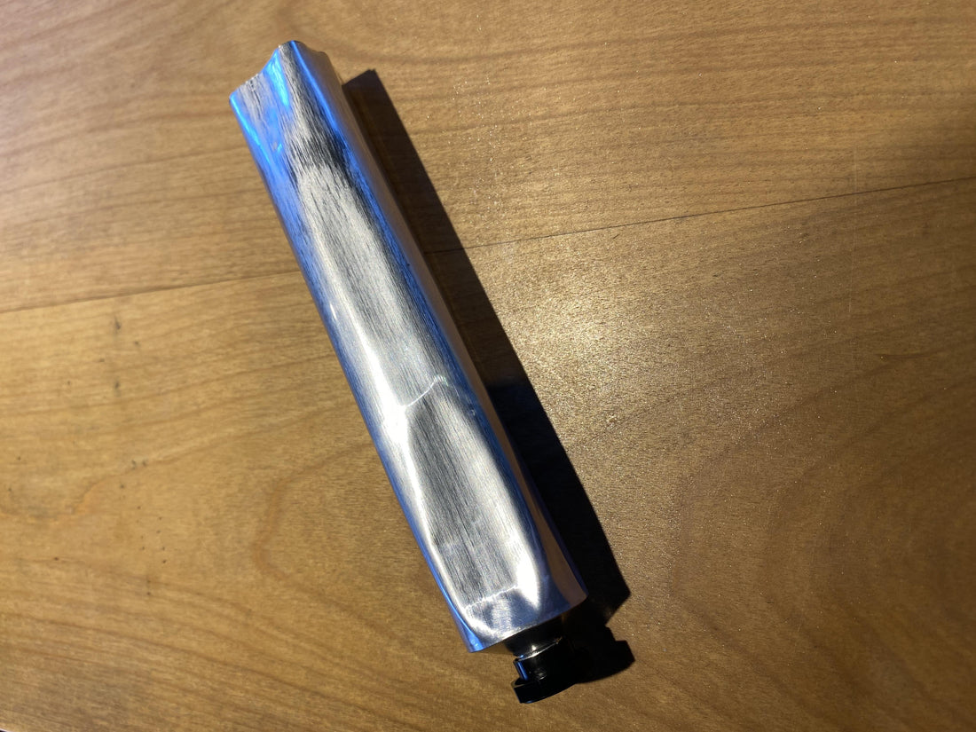 One slightly dented aluminum paint tube on a wooden surface.