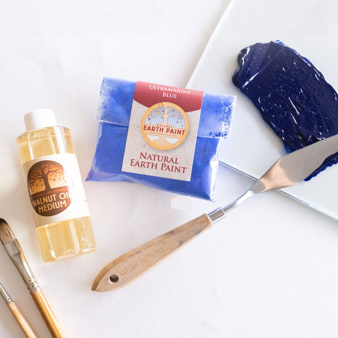 Bottle of walnut oil, pouch of ultramarine blue pigment, and the resulting glistening oil paint swatch 