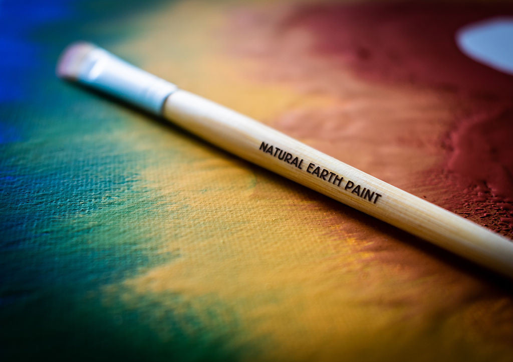 A branded paint brush lying on a canvas painted in rainbow colors