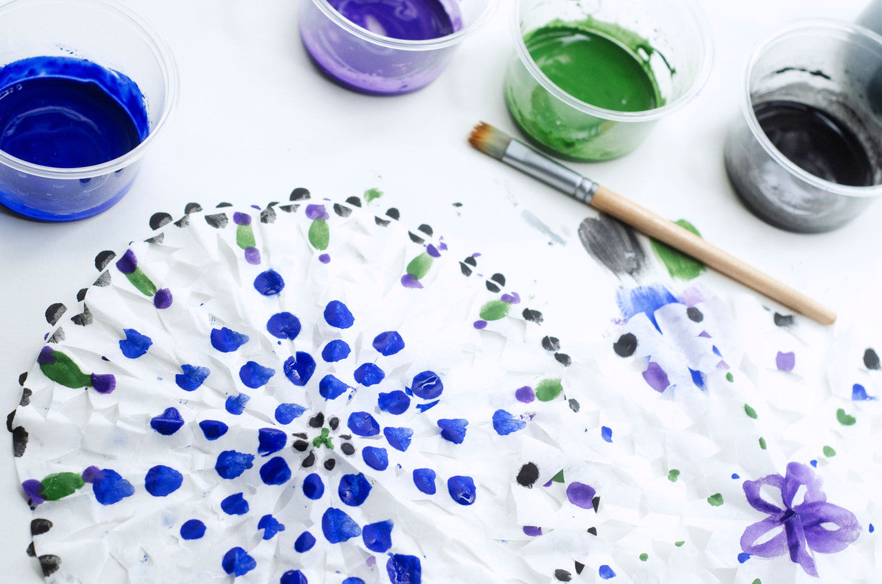 Four plastic cups of Natural Earth Paint, a paint brush and samples of painted paper snowflakes