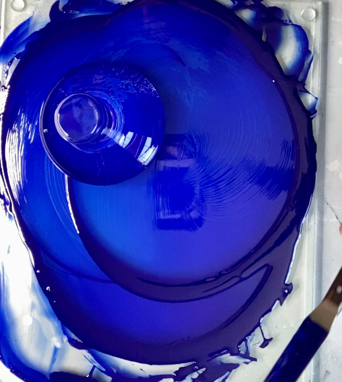 Blue oil paint being mixed with a glass muller on a glass palette