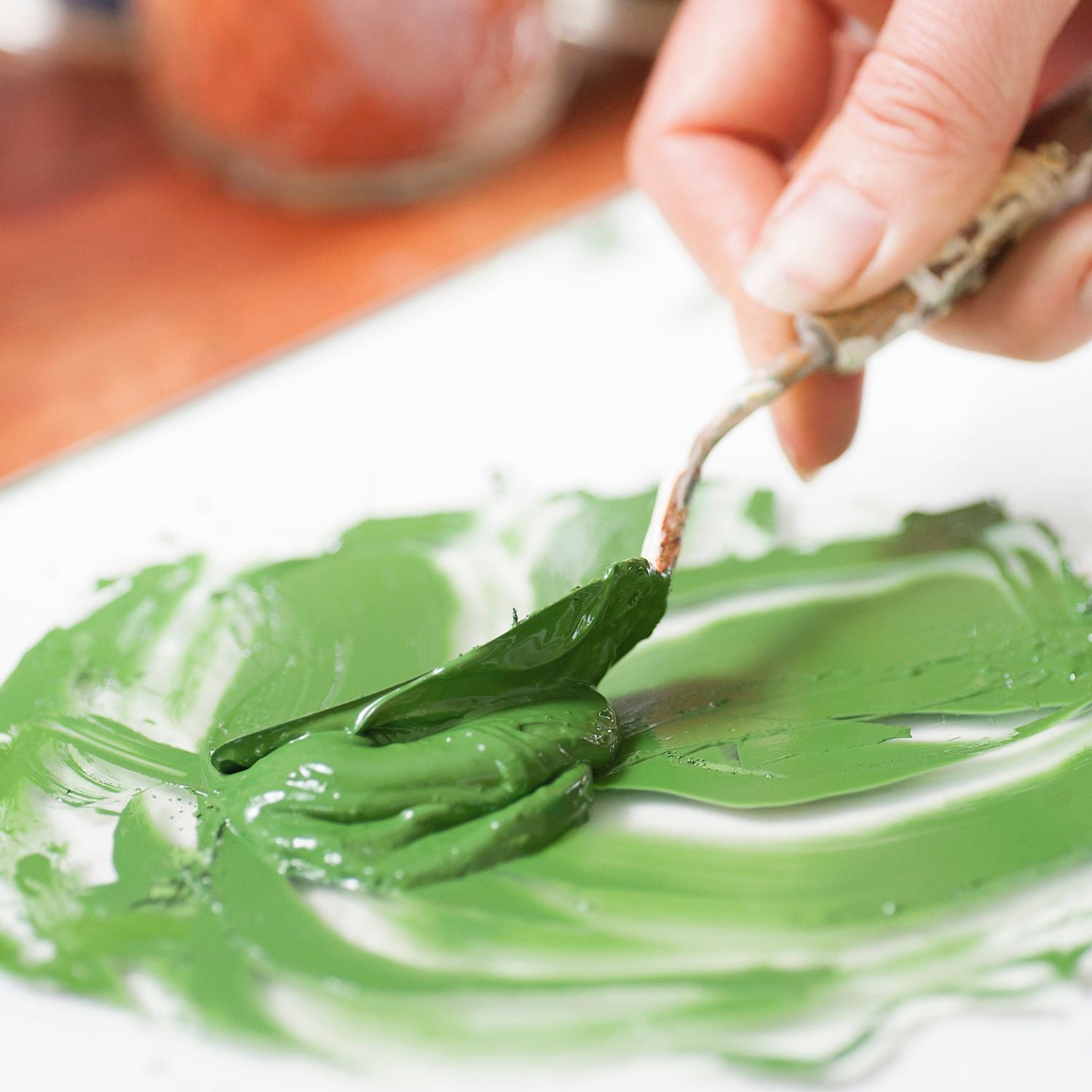A close up of green pigment and oil being mixed with a palette knife to make creamy natural oil paint.