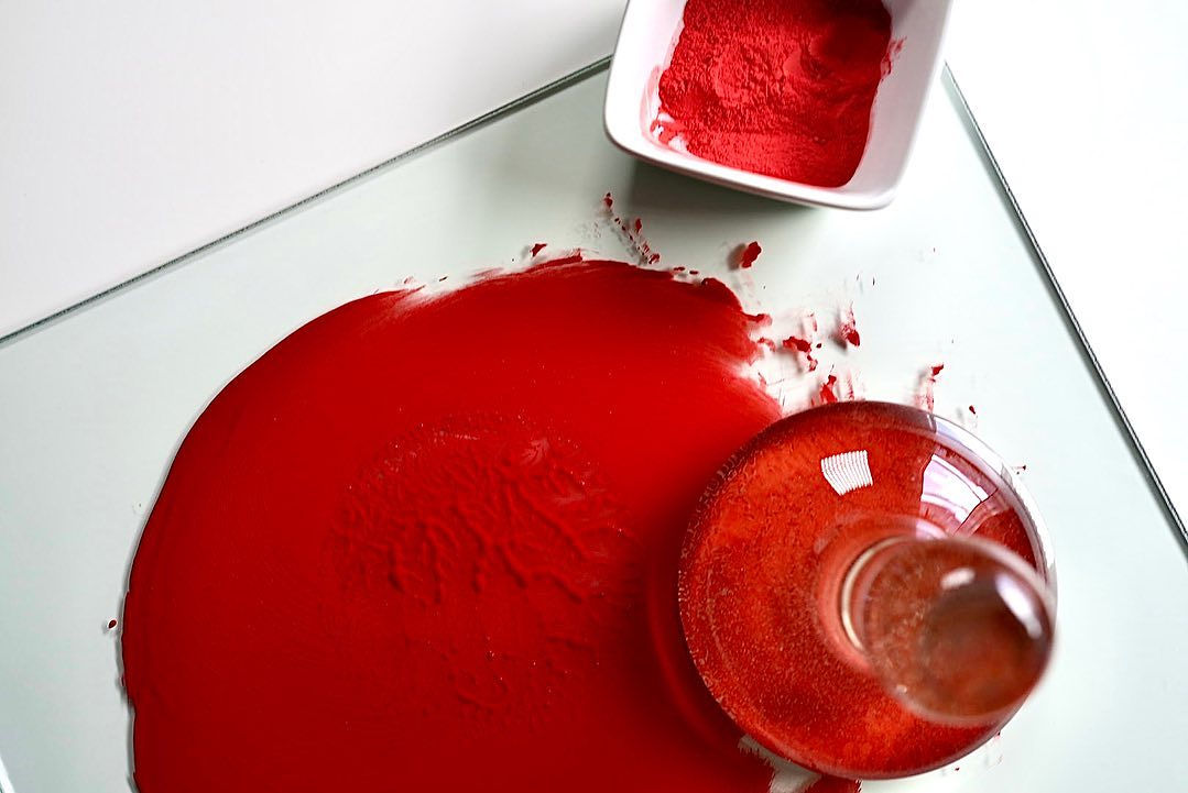 A glass muller mixing red pigment on a glass palette